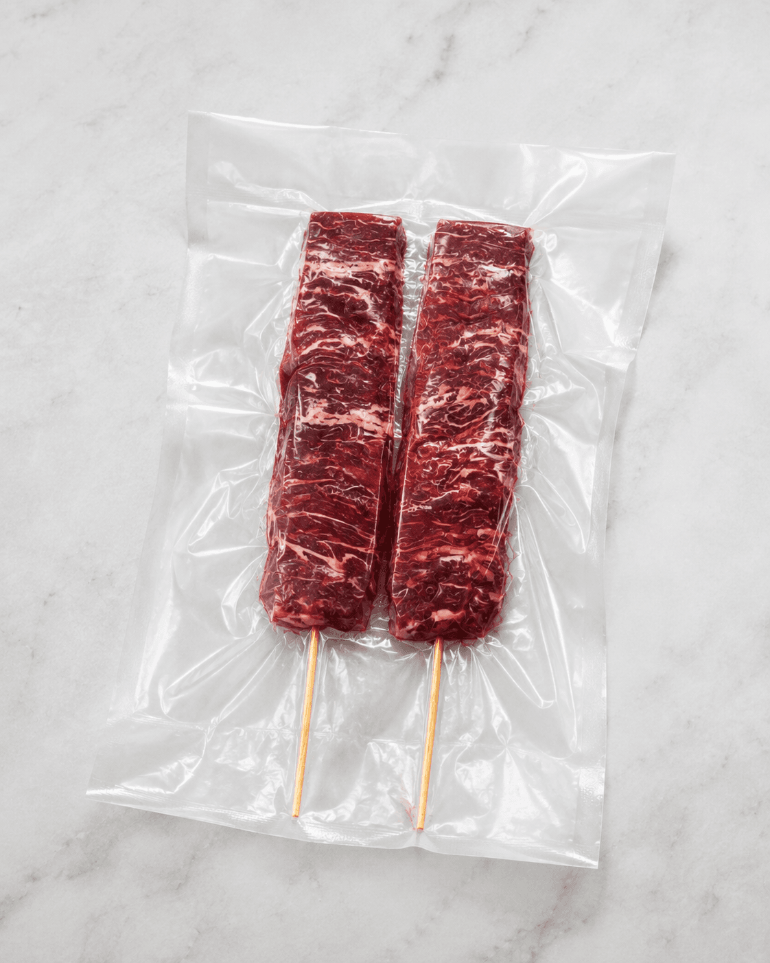 Dos brochetas crudas envasadas al vacío sobre mármol